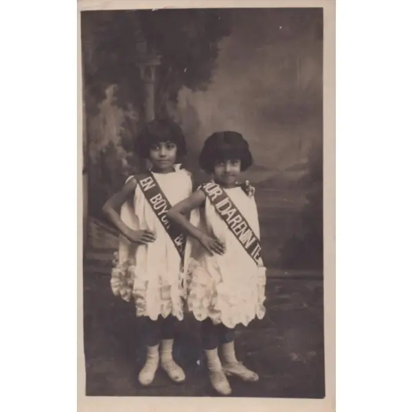 Bir millî bayram töreni için sloganlı kuşaklar takmış beyaz elbiseli iki küçük kızın stüdyo hatıra fotoğrafı, 9x14 cm